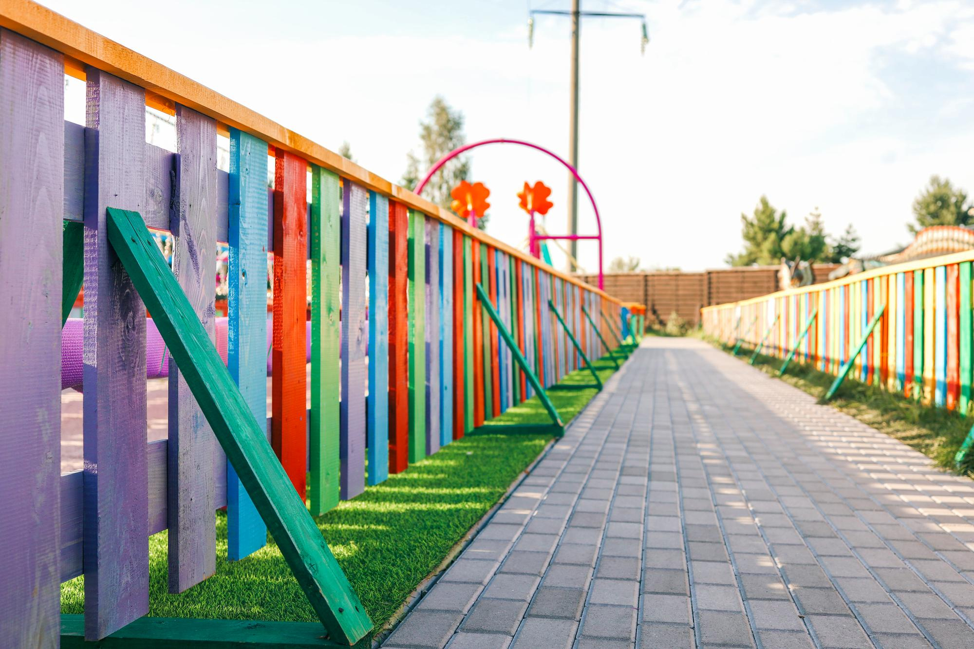 Colorful playground fencing with vertical slats in purple, red, and green, alongside a paved pathway, enhancing child-safe play environments in Yorkshire.