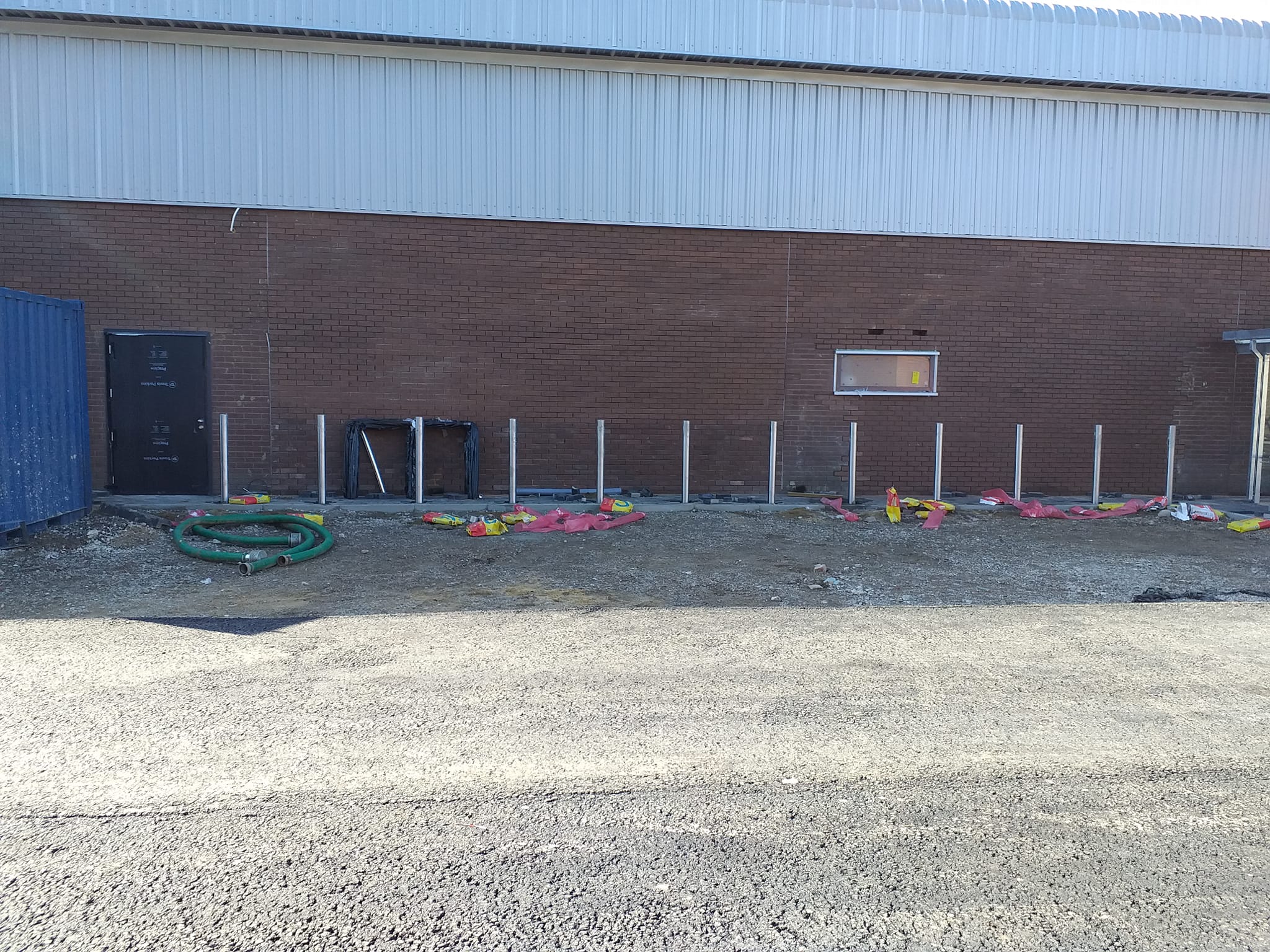 Installation site for street furniture, featuring concrete bollard foundations, construction materials, and a brick wall backdrop, indicative of urban infrastructure development.