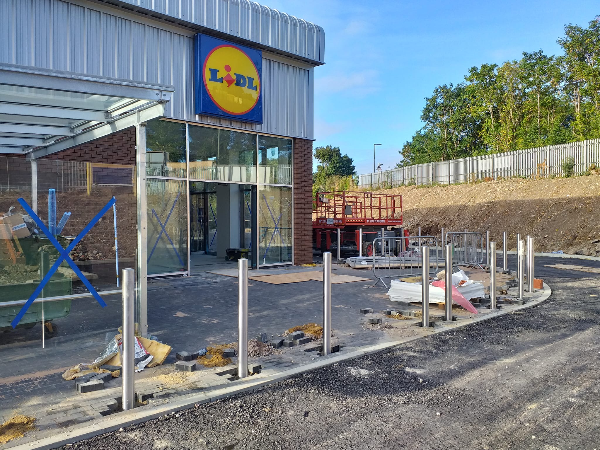 Lidl store entrance under construction with installed stainless steel bollards, construction debris, and safety barriers in urban setting.