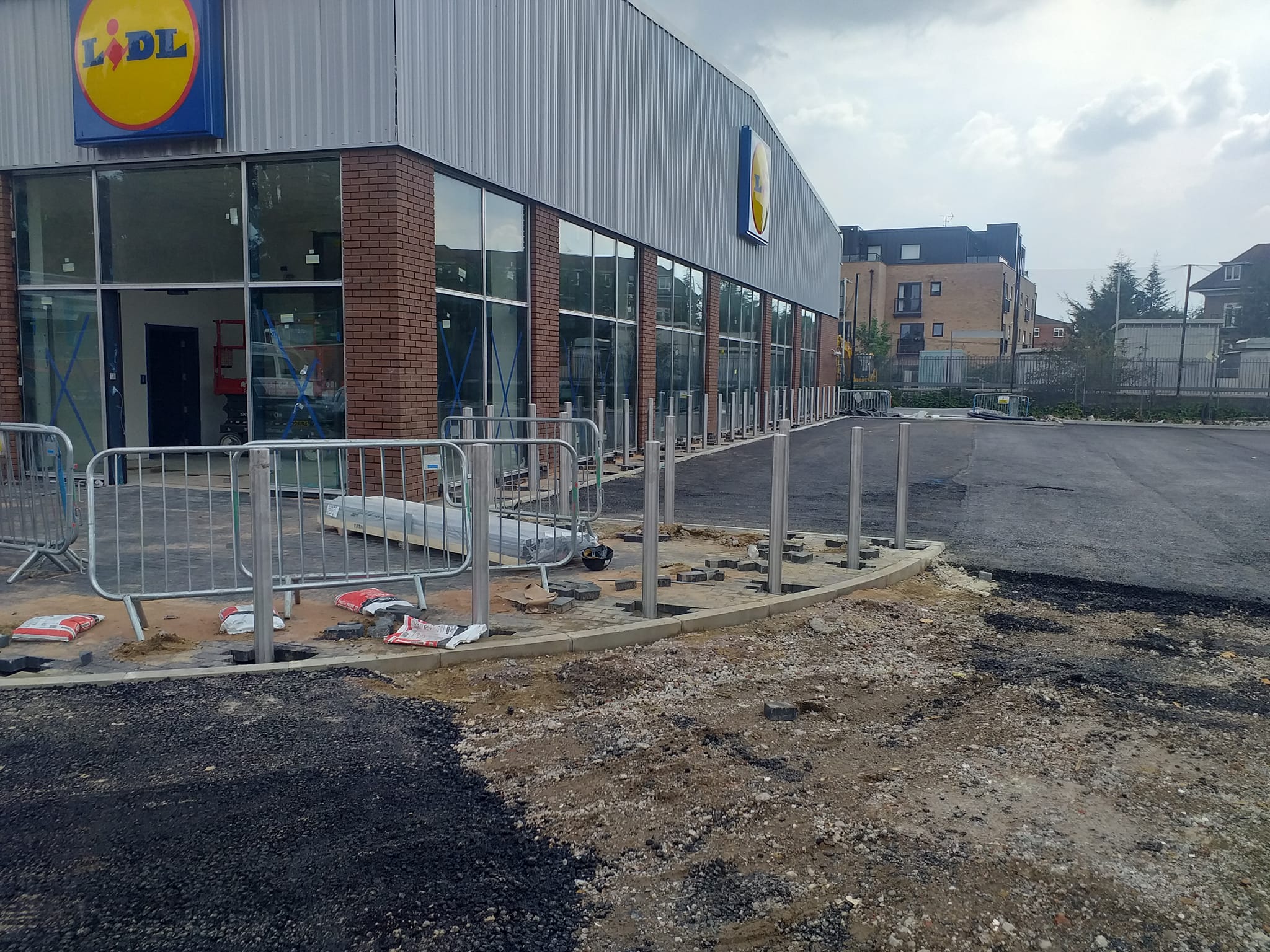 Construction site of Lidl store featuring pedestrian guardrails, bollard installations, and ongoing pavement work.