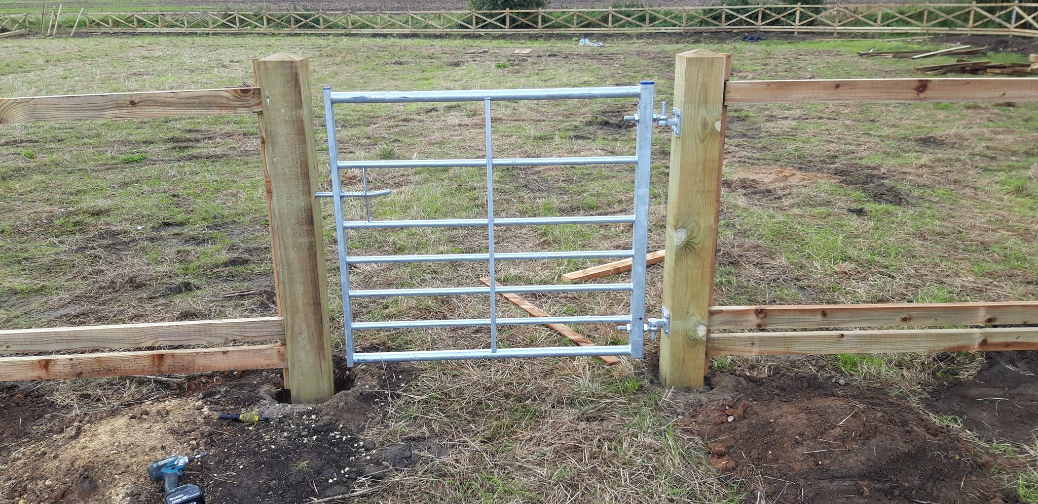 Galvanised steel farm gate installed between wooden posts in a grassy field, showcasing durability and functionality for rural access.
