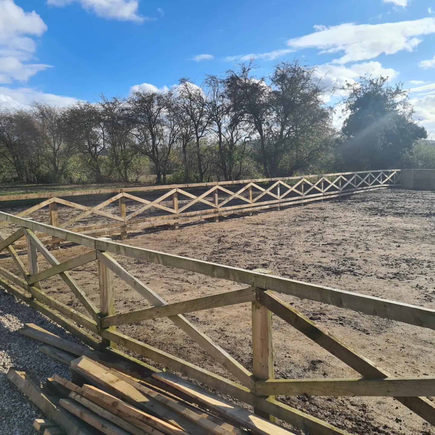 Wooden security fencing enclosing a cleared area, featuring diagonal cross bracing, surrounded by trees under a blue sky, illustrating effective perimeter solutions for agricultural or commercial properties.