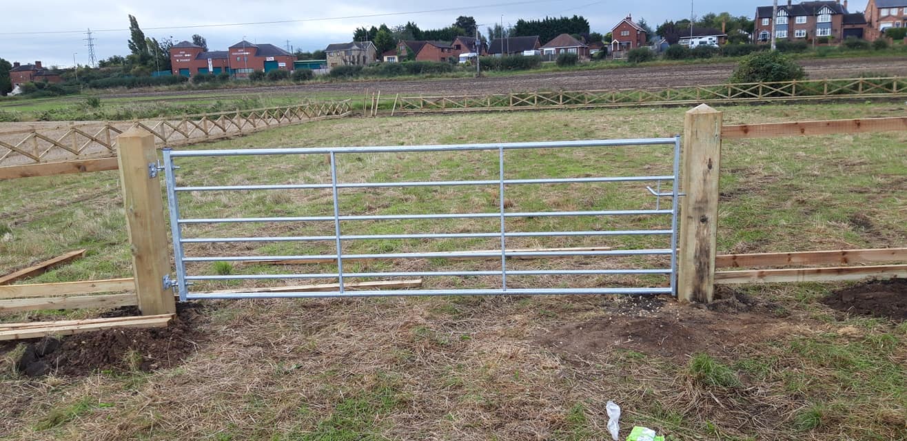 Galvanized steel gate installed on a wooden post fence in an agricultural setting, showcasing boundary demarcation for land management.