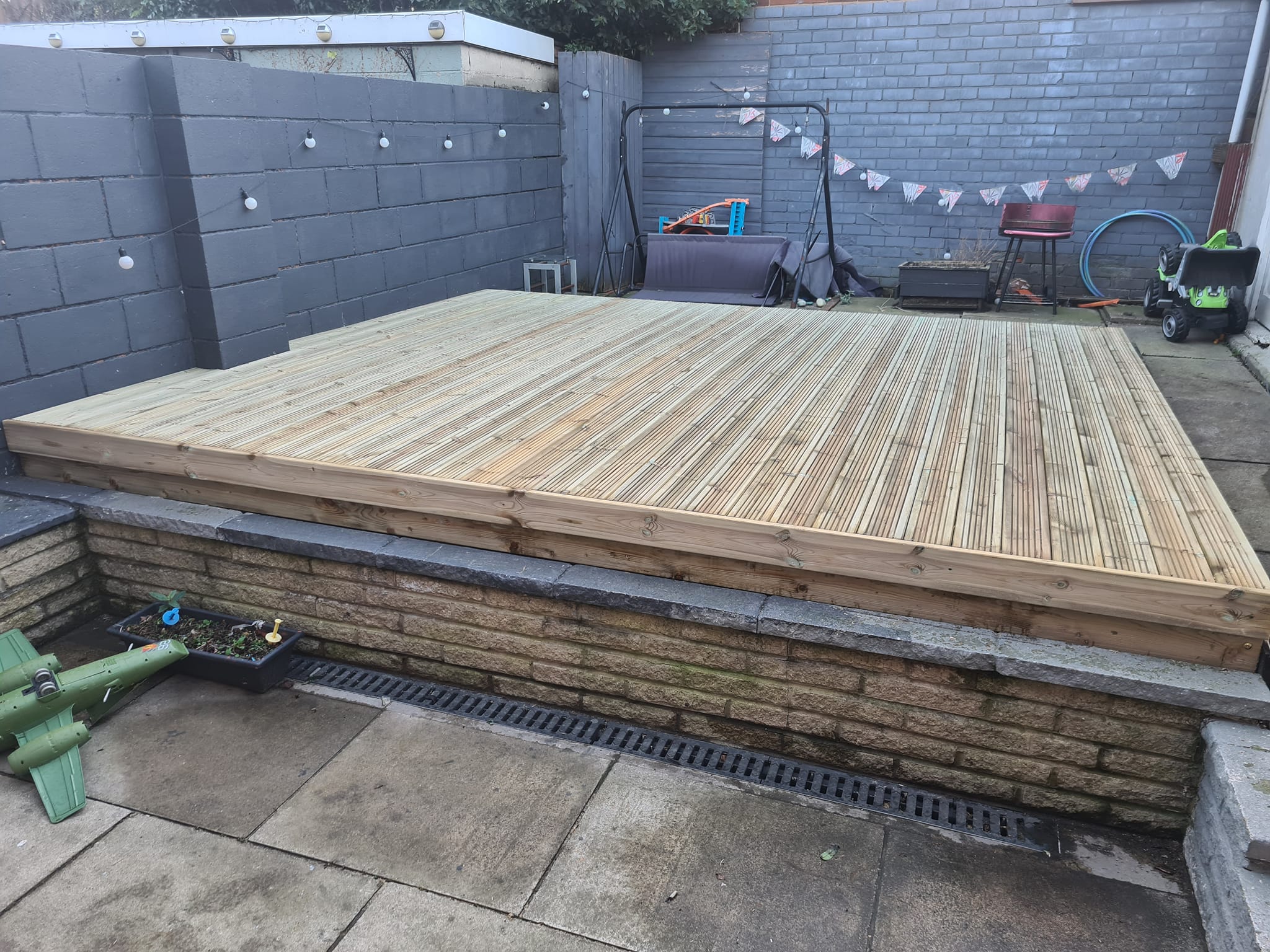Wooden decking installed in a garden setting, featuring a level surface with surrounding stone walls and outdoor decor, illustrating high-quality decking solutions by CK Fencing Contractors.