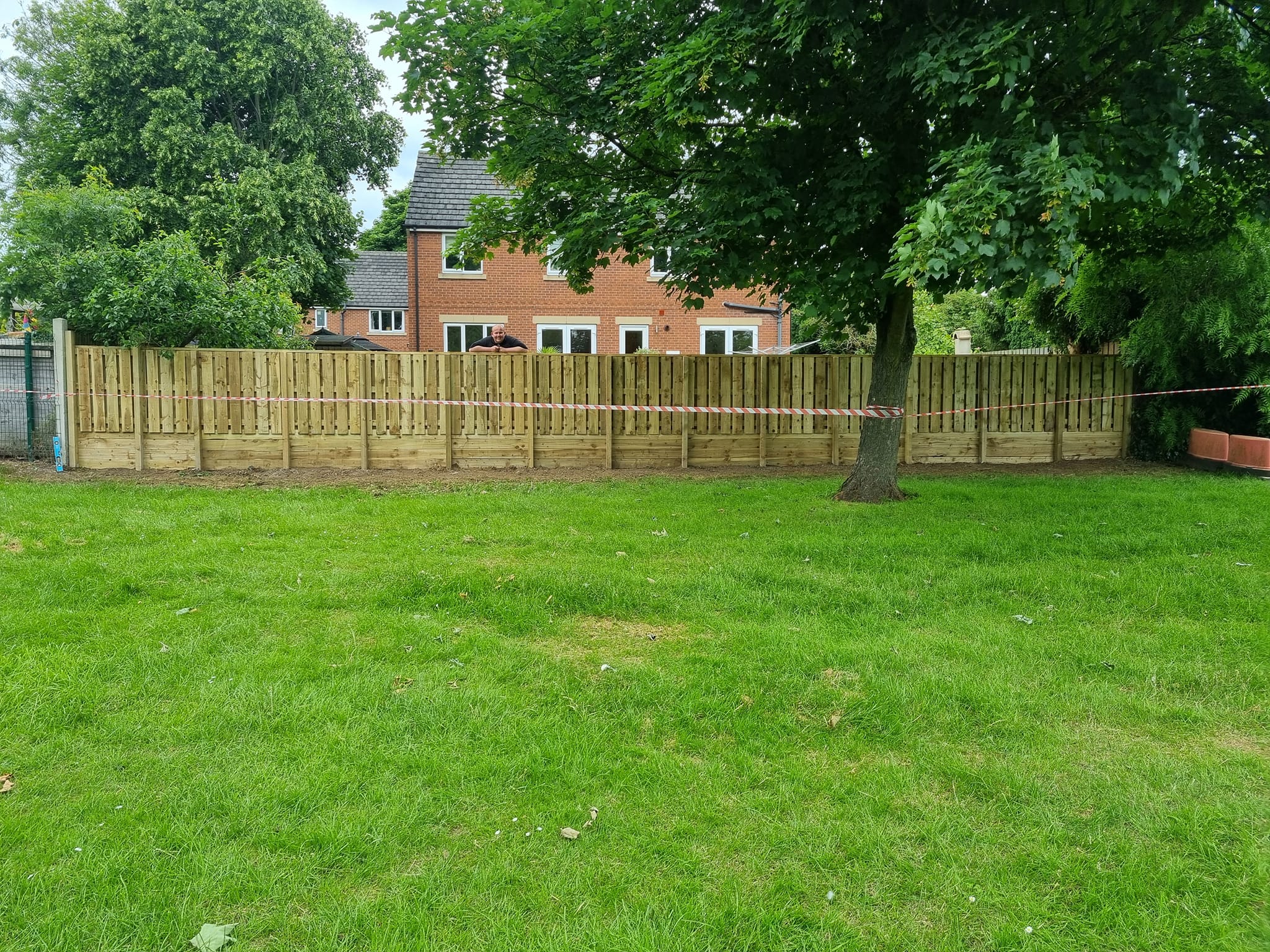 Newly installed wooden fencing with a man overseeing the work, set in a grassy area near residential homes, showcasing CK Fencing Contractors' domestic garden fencing services.