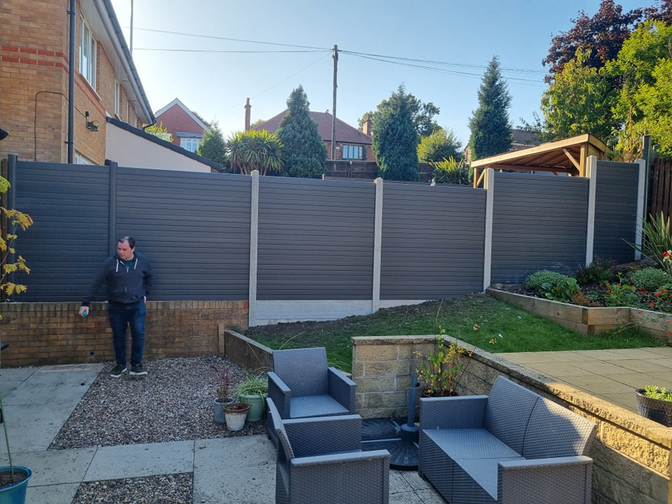 Man standing beside newly installed modern garden fencing in a residential backyard, showcasing secure and stylish fencing solutions.