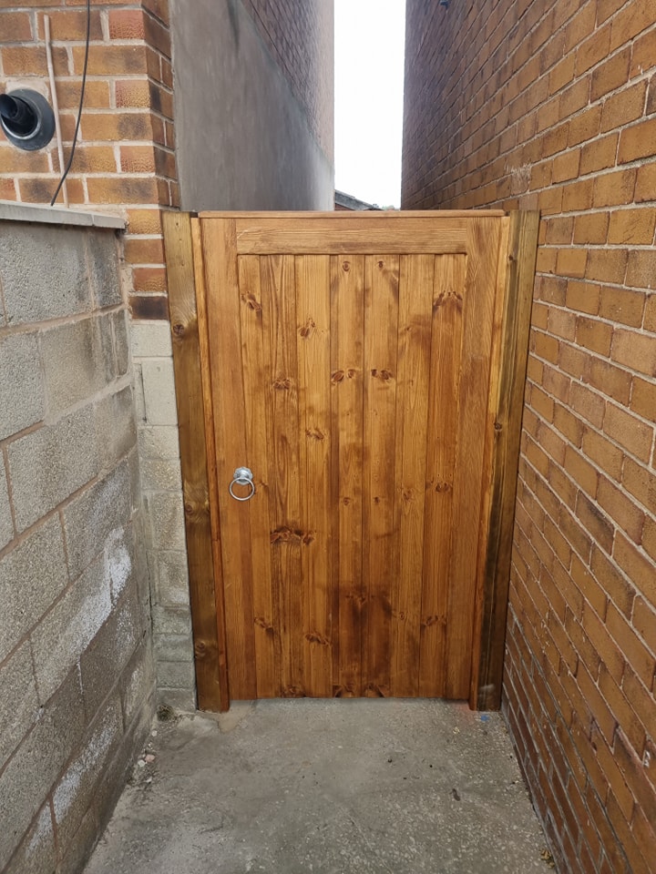 Wooden pedestrian access gate in narrow alleyway, showcasing durable construction and aesthetic appeal, relevant to CK Fencing Contractors' high-quality decking and fencing solutions.