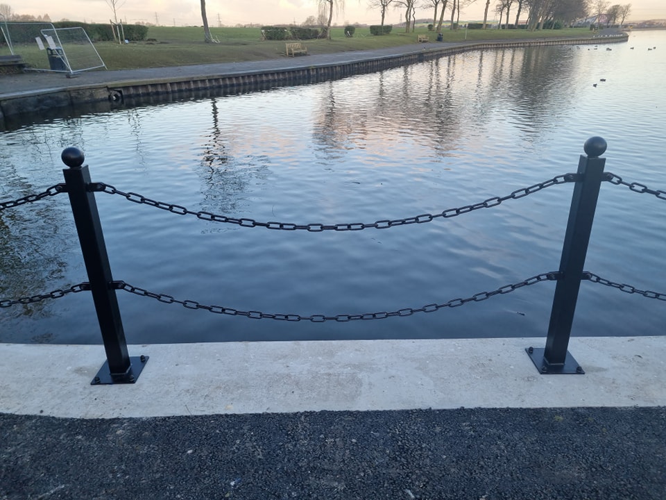 Black chain link fence along a waterway, providing safety and structure in public space, relevant to CK Fencing Contractors' street furniture installation services.