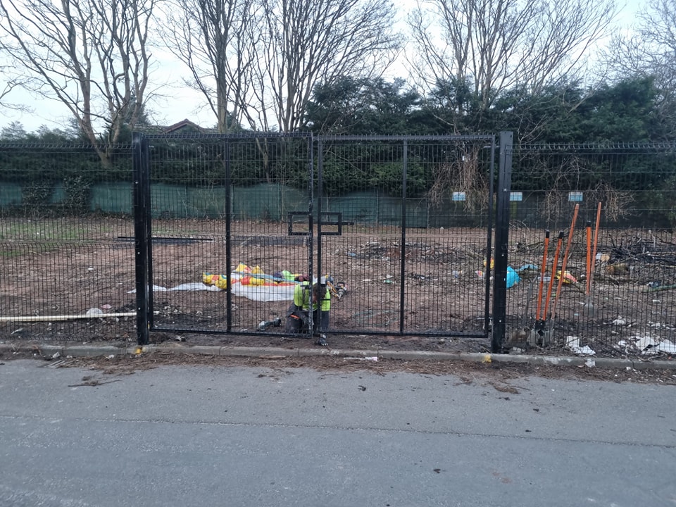 MUGA fencing gate with construction workers in high-visibility vests, surrounded by a cleared area with debris, emphasizing durable sports-specific fencing solutions for training grounds.