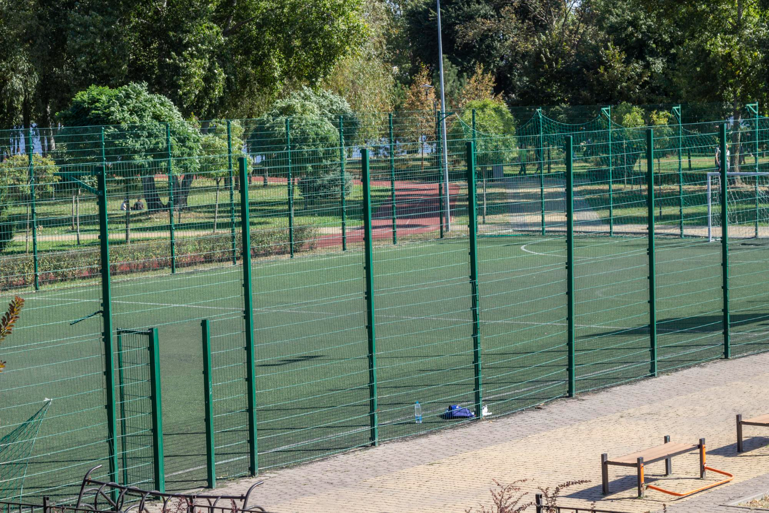 Multi-use games area fencing surrounding a synthetic pitch, featuring green metal mesh panels and a well-maintained playing surface, emphasizing durability and safety for sports activities.