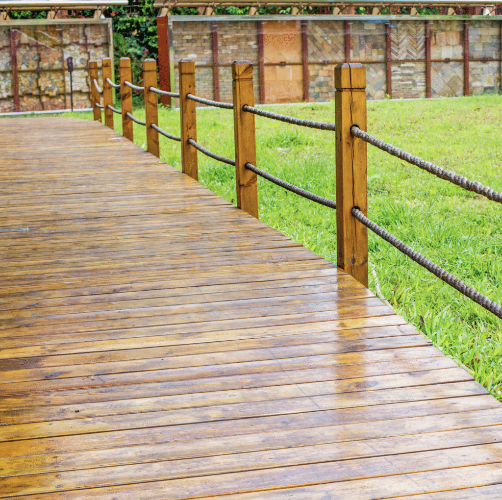 Wooden pathway deck with rope railing, surrounded by lush green grass, showcasing a natural aesthetic for outdoor spaces.