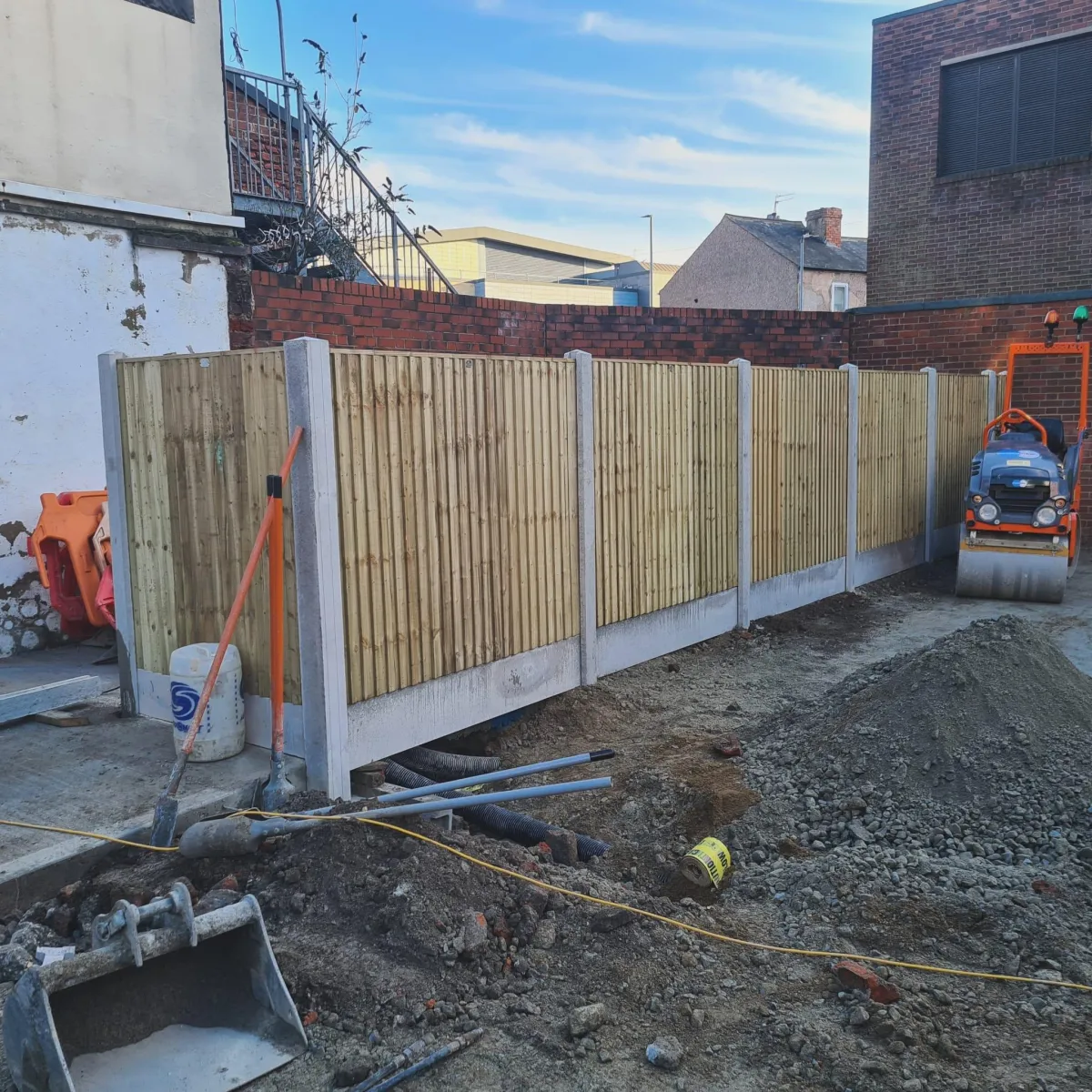 Fencing installation with wooden panels and concrete posts, construction site featuring machinery and tools, showcasing CK Fencing Contractors' recent project in Wakefield.