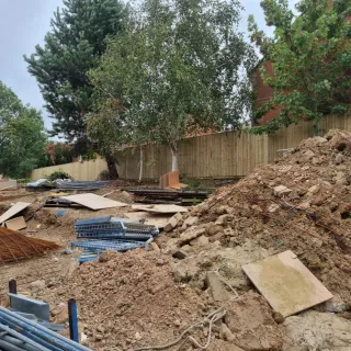 Construction site featuring earthworks, construction materials, and a wooden fence in the background, showcasing CK Fencing Contractors' ongoing project for site hoarding solutions.