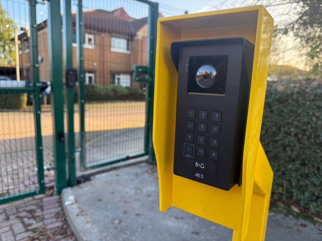 Automated access control panel with keypad and intercom, positioned near green security gates in a residential area, highlighting fencing and gate solutions provided by CK Fencing Contractors.