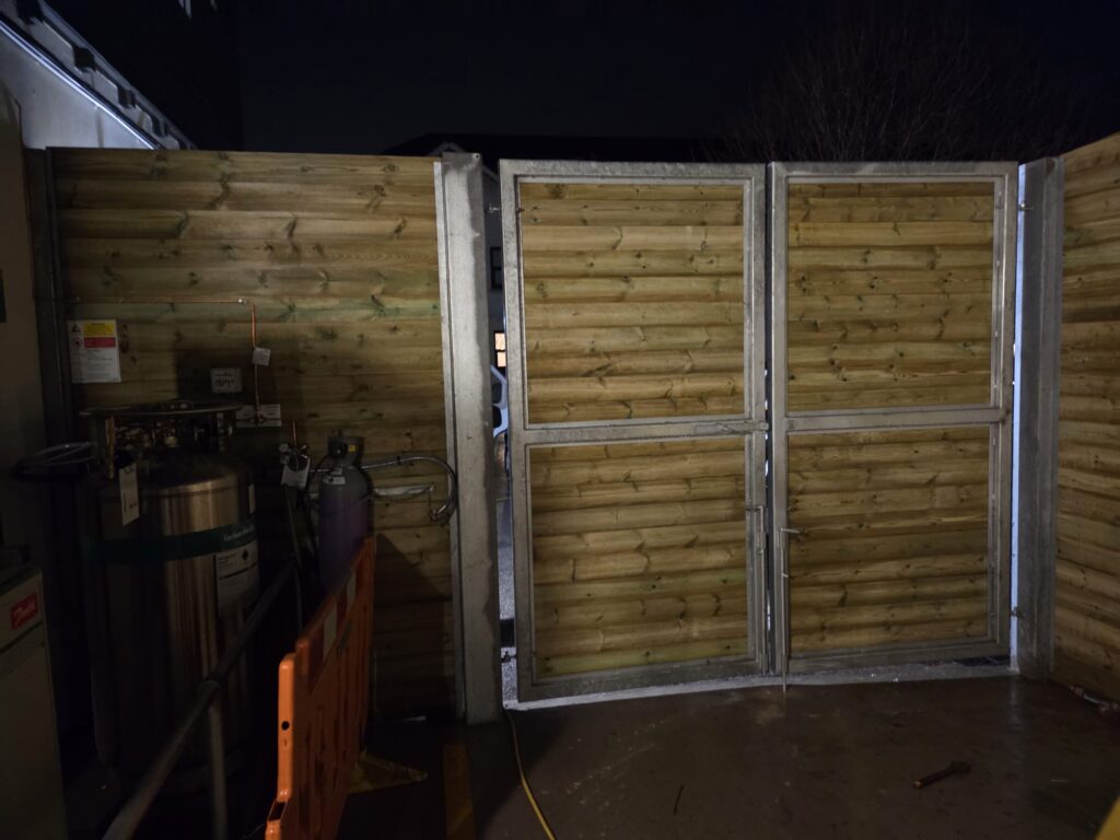 Site hoarding installation with double gates, featuring wooden panels and metal framing, showcasing a secure compound area for commercial use.