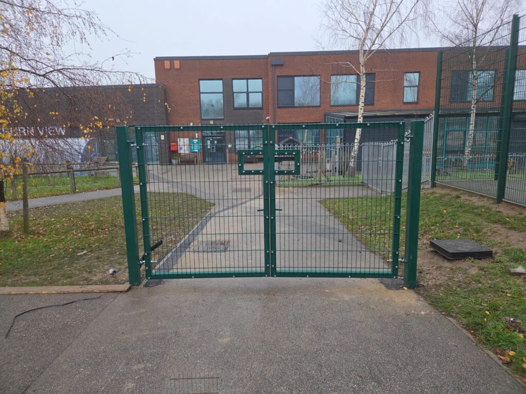 Double leaf gate at Faurburn View Primary School, featuring twin mesh design, leading to a pathway, surrounded by grass and trees, emphasizing secure access for educational facilities.